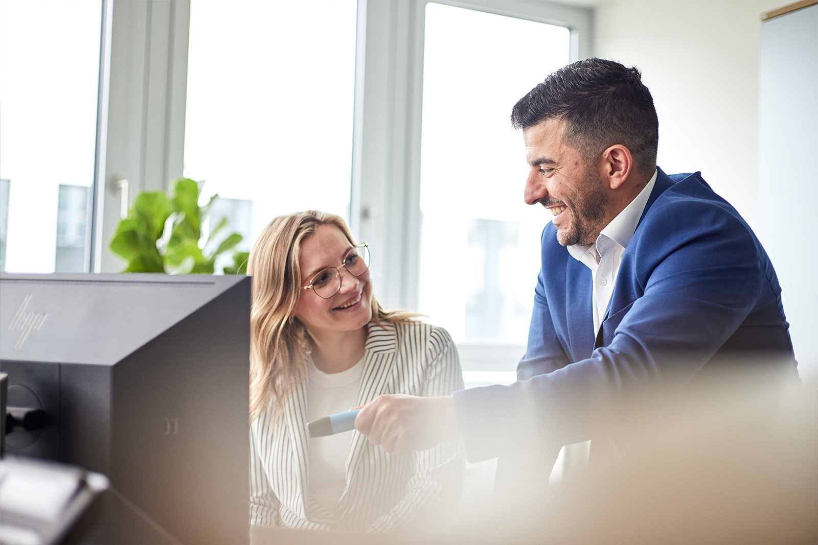 Zwei TriFinance Project Consultants besprechen in München lächelnd Finanzdaten für das Financial Reporting am Monitor.
