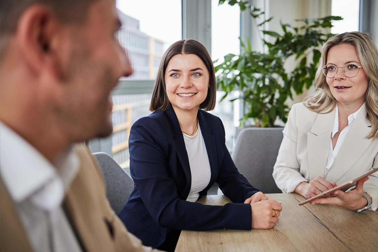 Zwei lächelnde TriFinance Consultants im Kölner Büro beim Karriere-Gespräch am Tisch mit einem Kandidaten für den Einstieg im Accounting.