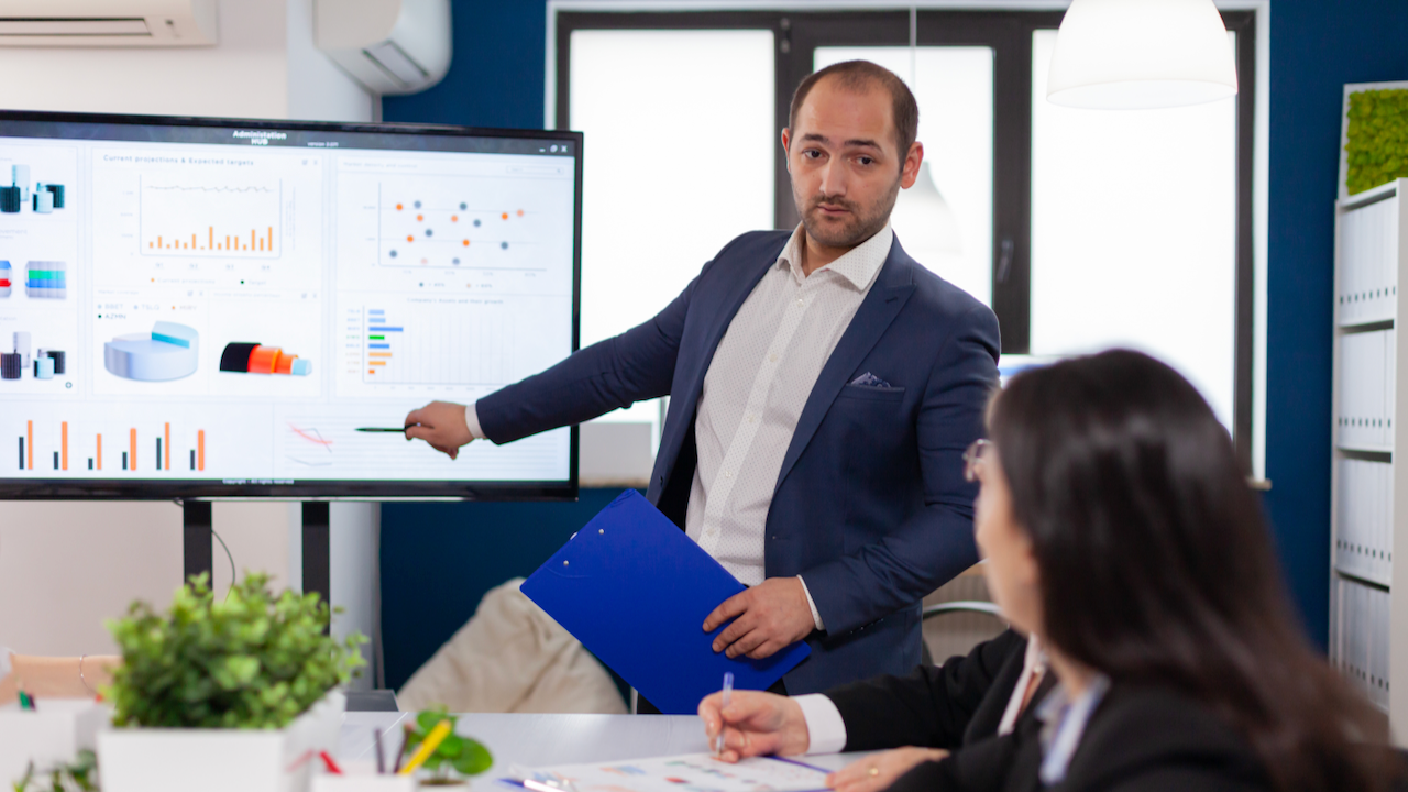 Successful team leader briefing pointing explaining project in conference room brainstorming. Corporate staff discussing new business application with colleagues looking at screen