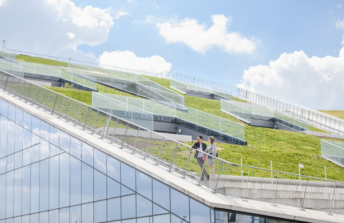 Two professionals discussing strategy outside a modern glass building with a sloped green roof, illustrating that organizational AI readiness relies heavily on a strong human foundation.